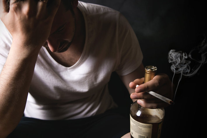 Desperate man sitting with bottle of alcohol and marijuana